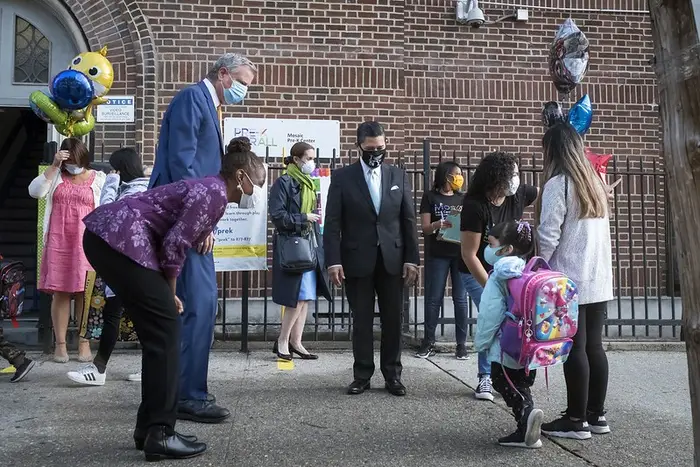 (L-R) First Lady Chirlane McCray bends down as she sees a girl holding an adult's hand outside a school in Queens. Next to McCray is her husband, Mayor Bill de Blasio, and Schools Chancellor Richard Carranza, who also look at the little girl heading to the Mosaic Pre-K Center in Queens for the first day of in-person learning at public schools last month.